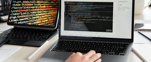 A developer writing code on a laptop, displaying programming scripts in an office environment.